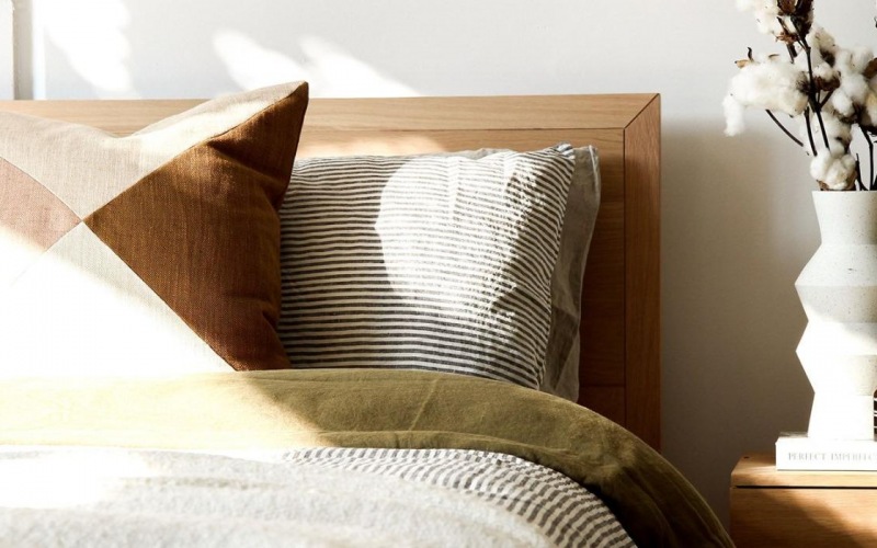 swath of sunlight shines across a well made bed and bedside table with a vase of cotton plants